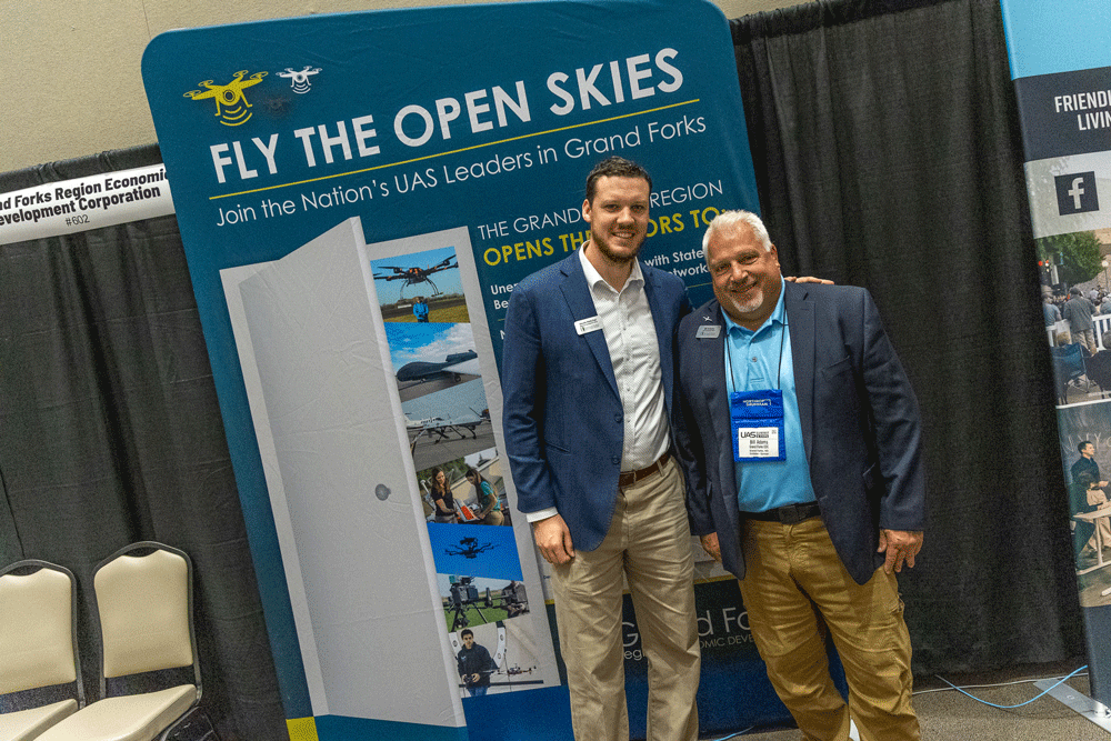 Kevin Hatcher and Bill Adams stand together in front of the Grand Forks Region EDC sign at the UAS Summit and Expo.