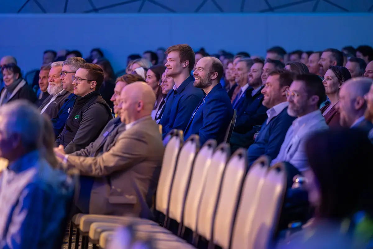 The audience sits in rows of seats smiling and laughing at the panelists on stage at the annual meeting.