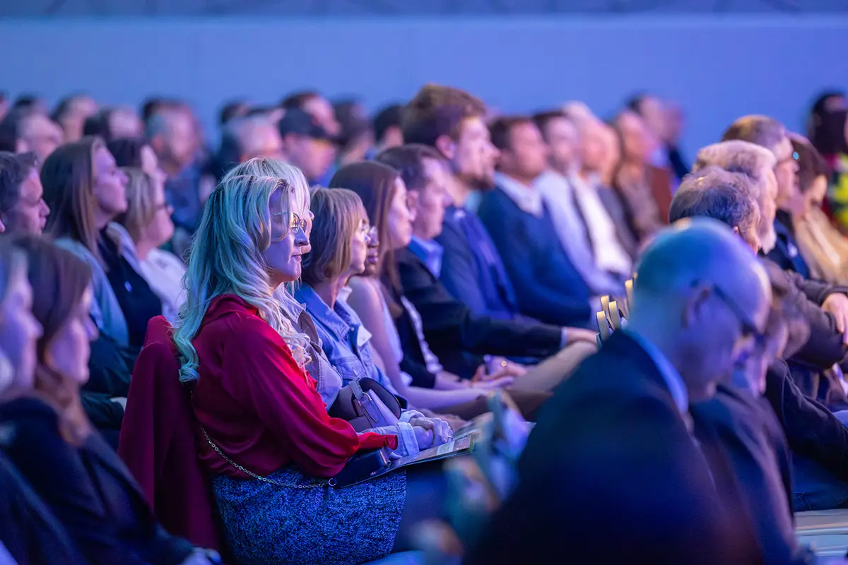 The audience sits in rows of seats smiling and laughing at the panelists on stage at the annual meeting.